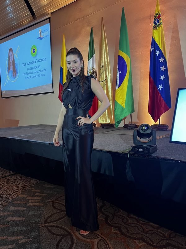 Dra. Amanda Vitorino em frente ao telão que a apresenta como conferencista, ao lado de bandeiras de países latino-americanos